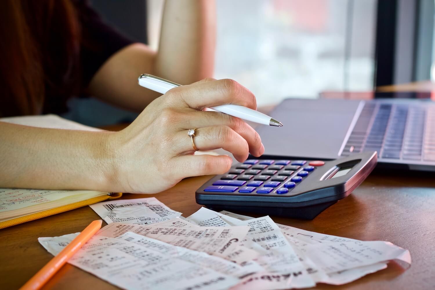 Hand mit Stift tippt auf einem Taschenrechner, daneben liegen Belege und ein Laptop – symbolisch für sorgfältige steuerliche Prüfung und Steuerberatung.